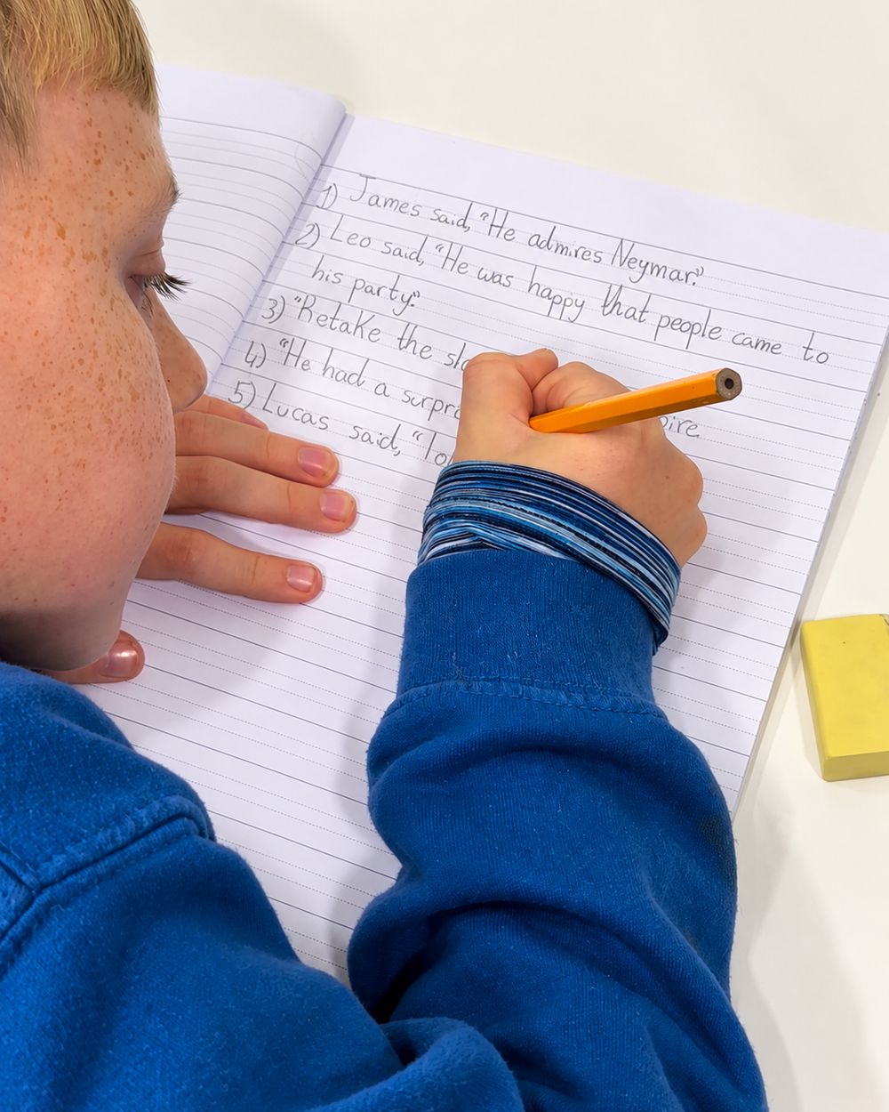A pupil writing sentences with speech marks in his jotter